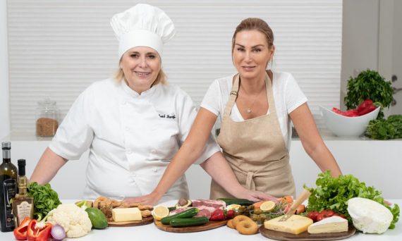 Two female chefs with variety of fresh ingredients in a kitchen setting, showcasing culinary preparation.